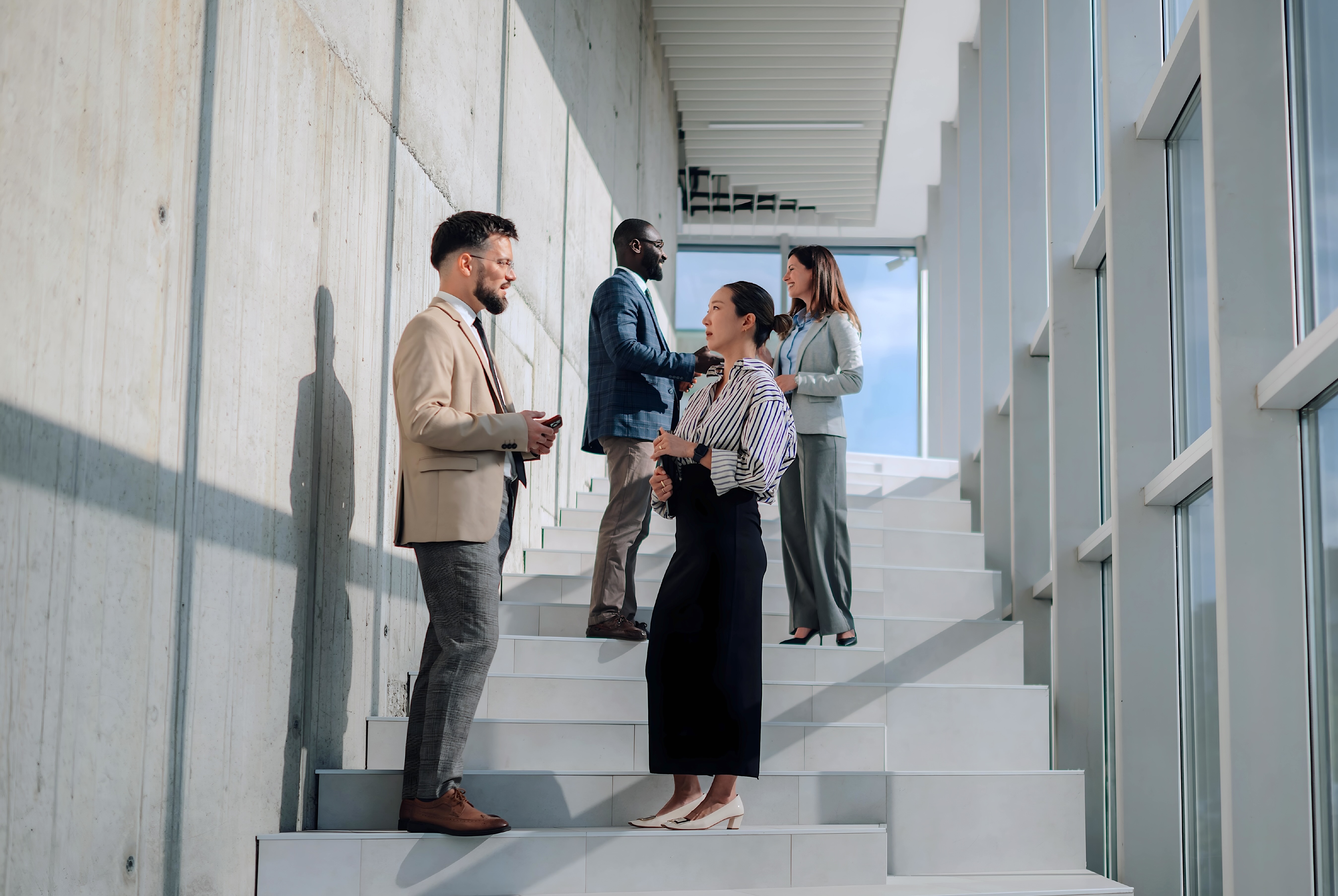 Business professionals networking and talking on modern office staircase with tall windows