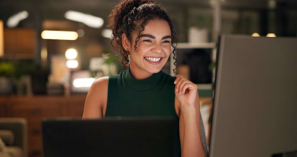 Woman in green top smiling while working at computer in warm office setting